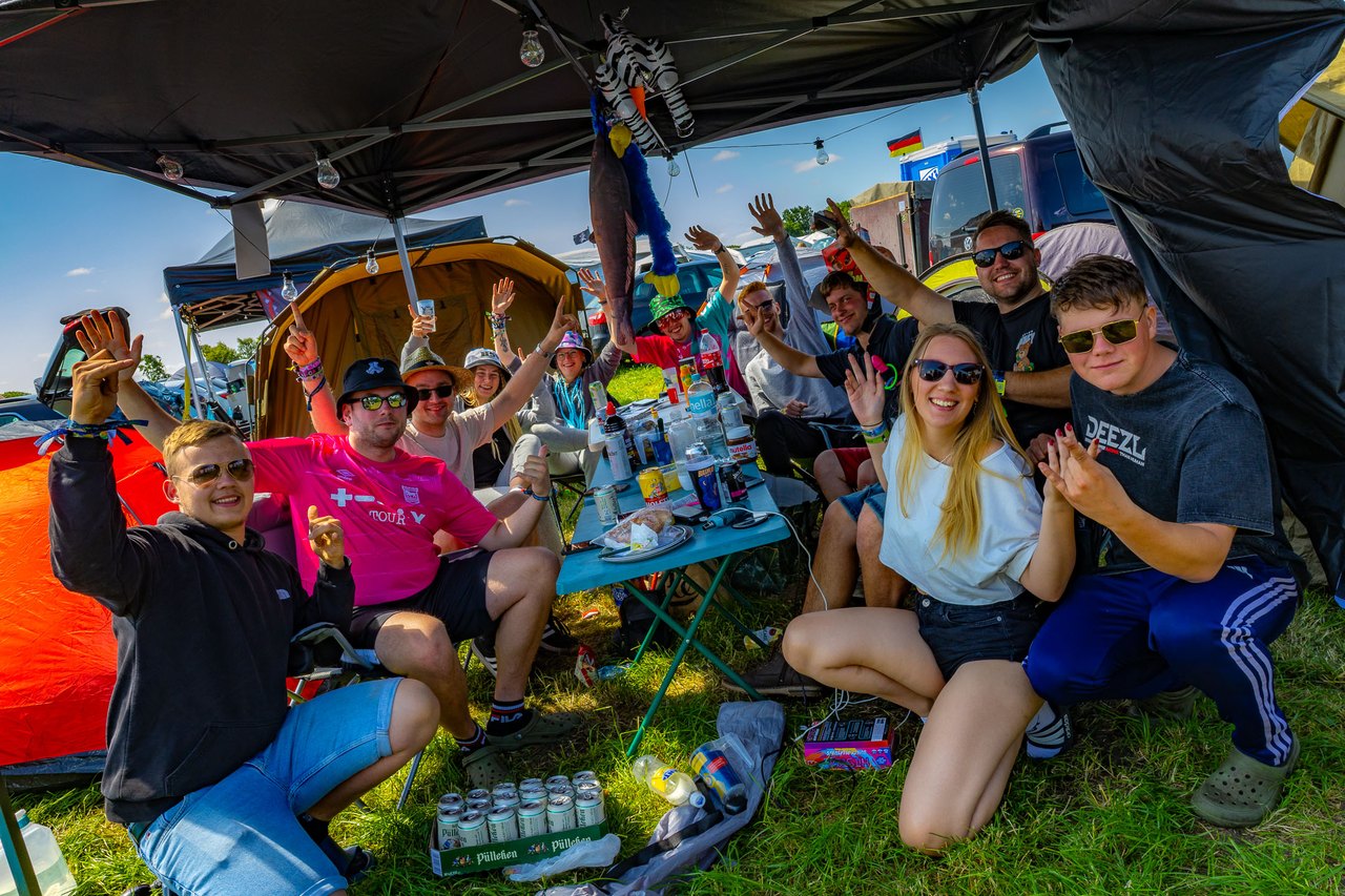 En gruppe venner sidder under en pavillon på campingpladsen med hænderne i vejret.